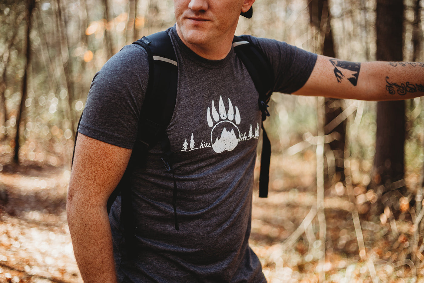 A hiker in the woods leaning against a tree wearing a Hike Life tee 
